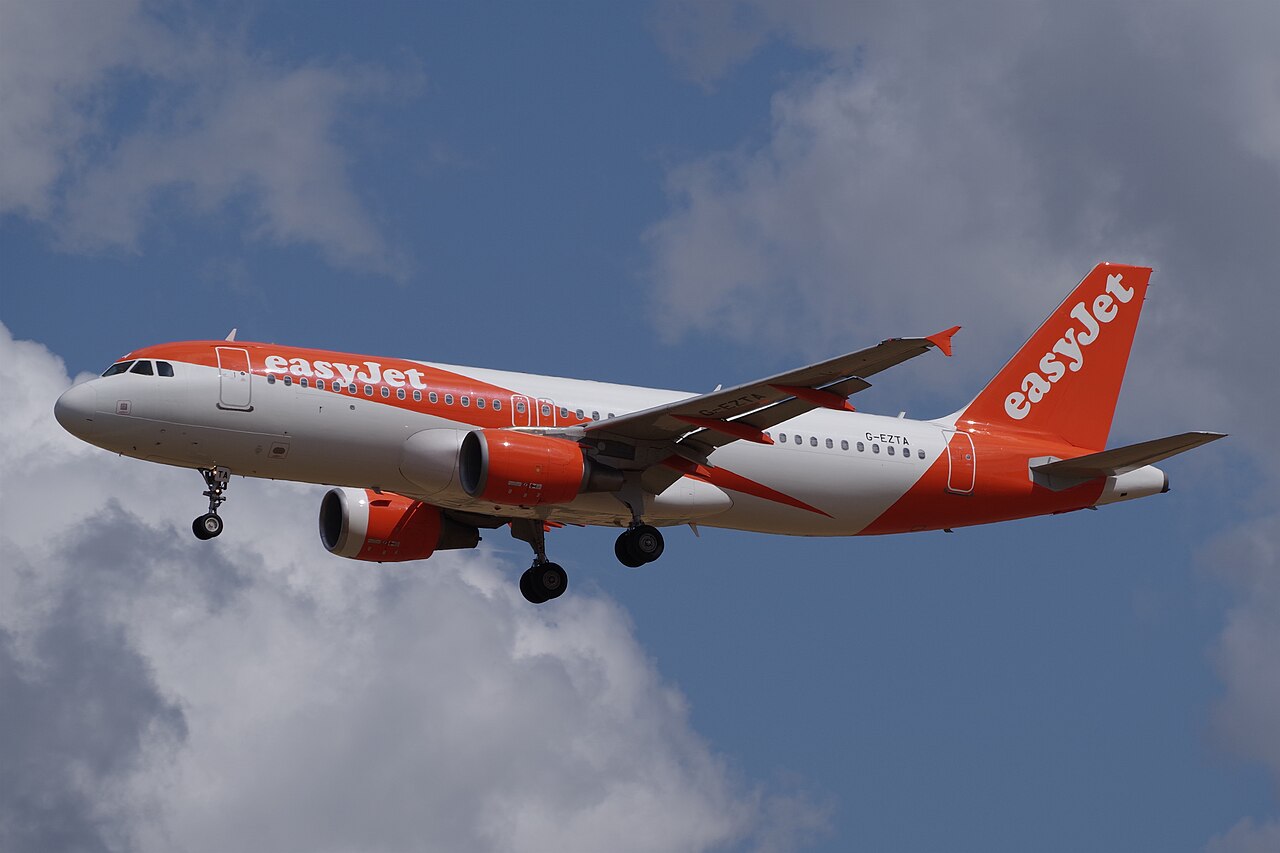Orange-and-white Airbus A320-214 G-EZTA approaching to land, with two underwing engines, wingtip fences and landing gear extended.