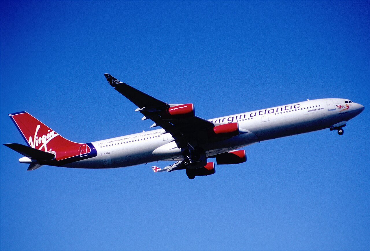 Virgin Atlantic A340 G-VBUS in flight, seen from below with four engines visible.