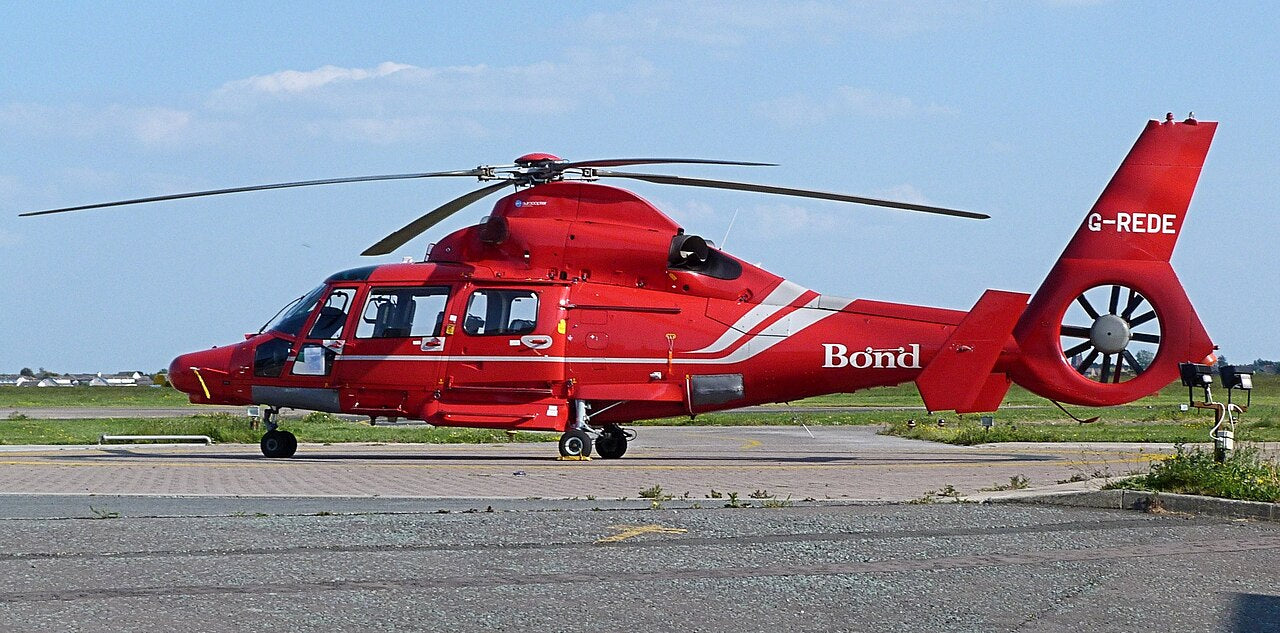 Red Dauphin parked sideways with the full visible main rotor, cockpit, cabin, wheels and enclosed tail rotor.