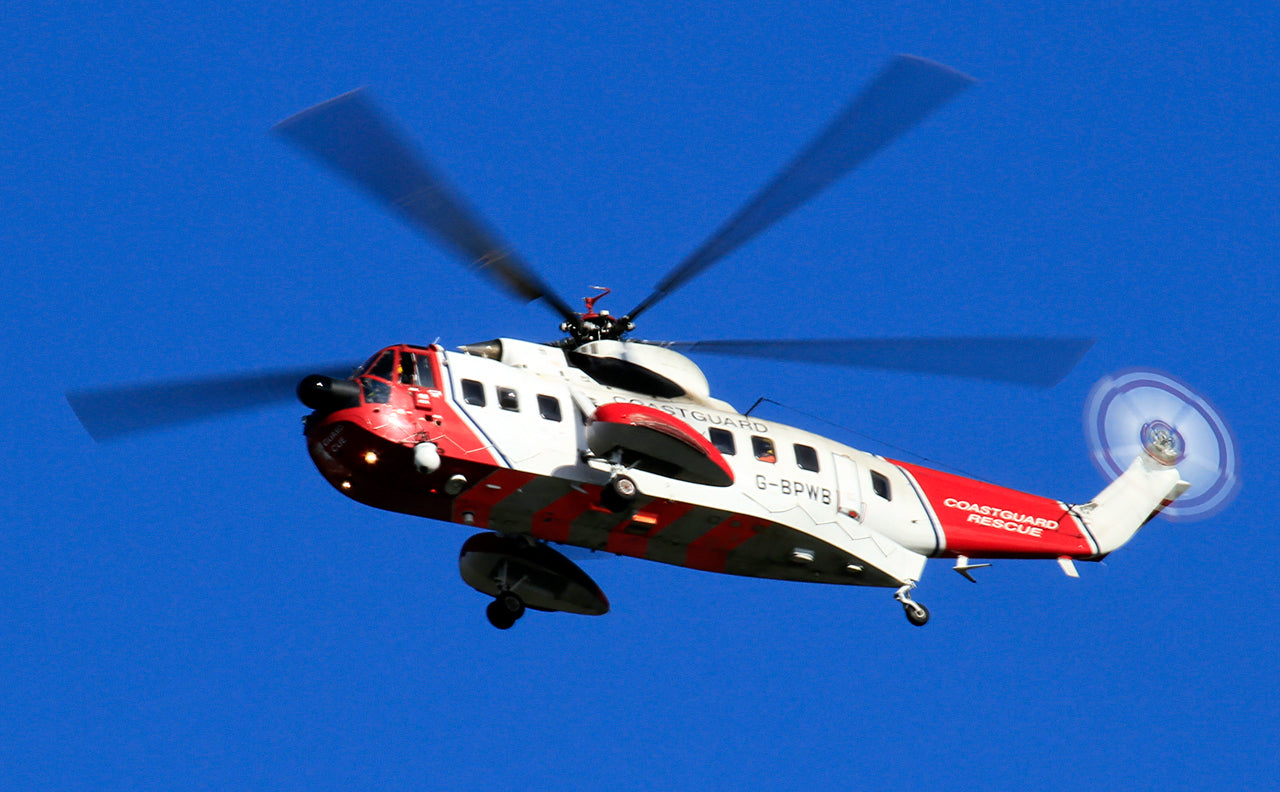 Red and white S-61N viewed from below and the side in flight, with a long cabin, side floats, landing gear and blurred rotating rotors.