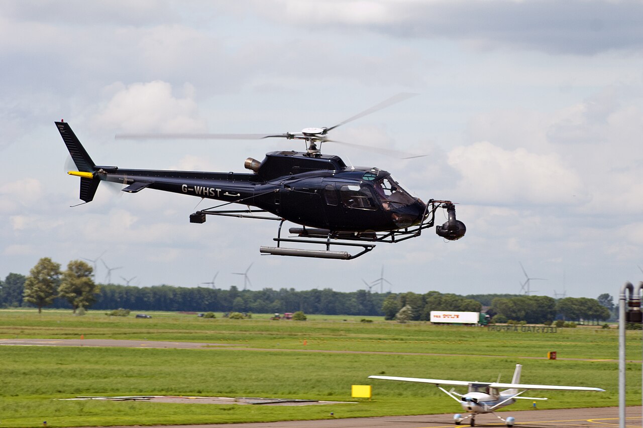 Dark AS350B2 G-WHST in flight, with skids, rotor, tail and a camera mounted in front.
