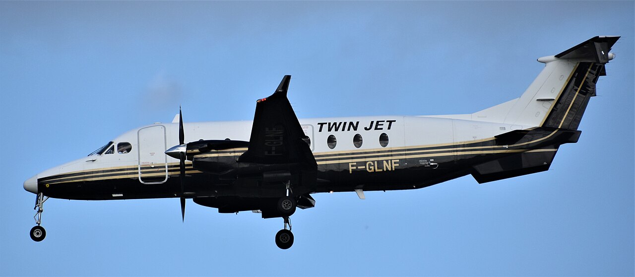 Twin Jet Beechcraft 1900D F-GLNF in flight with landing gear extended, showing the nose, propellers, wings and T-tail within the frame.
