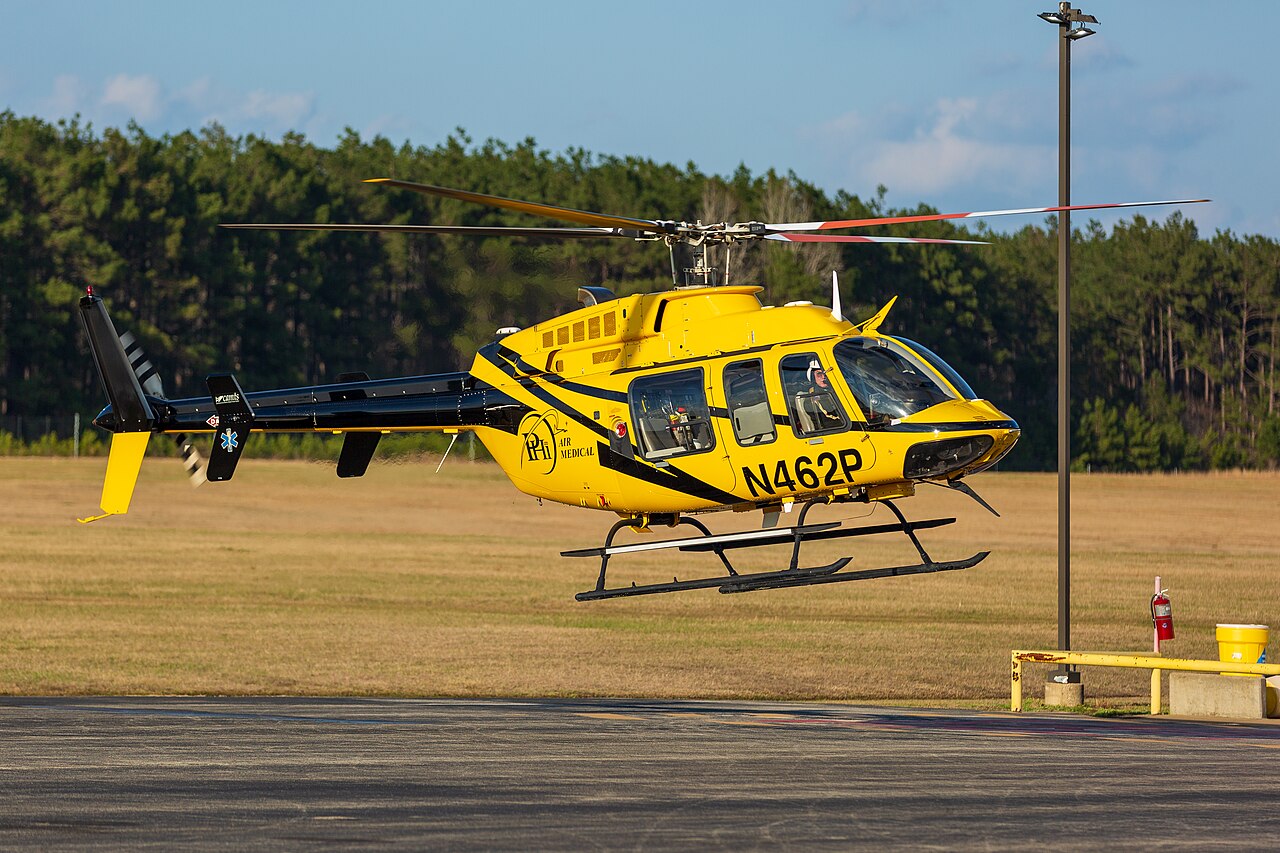 Yellow-and-black Bell 407 N462P hovering, with all visible main rotor blades, cabin, tail and skids inside the frame.