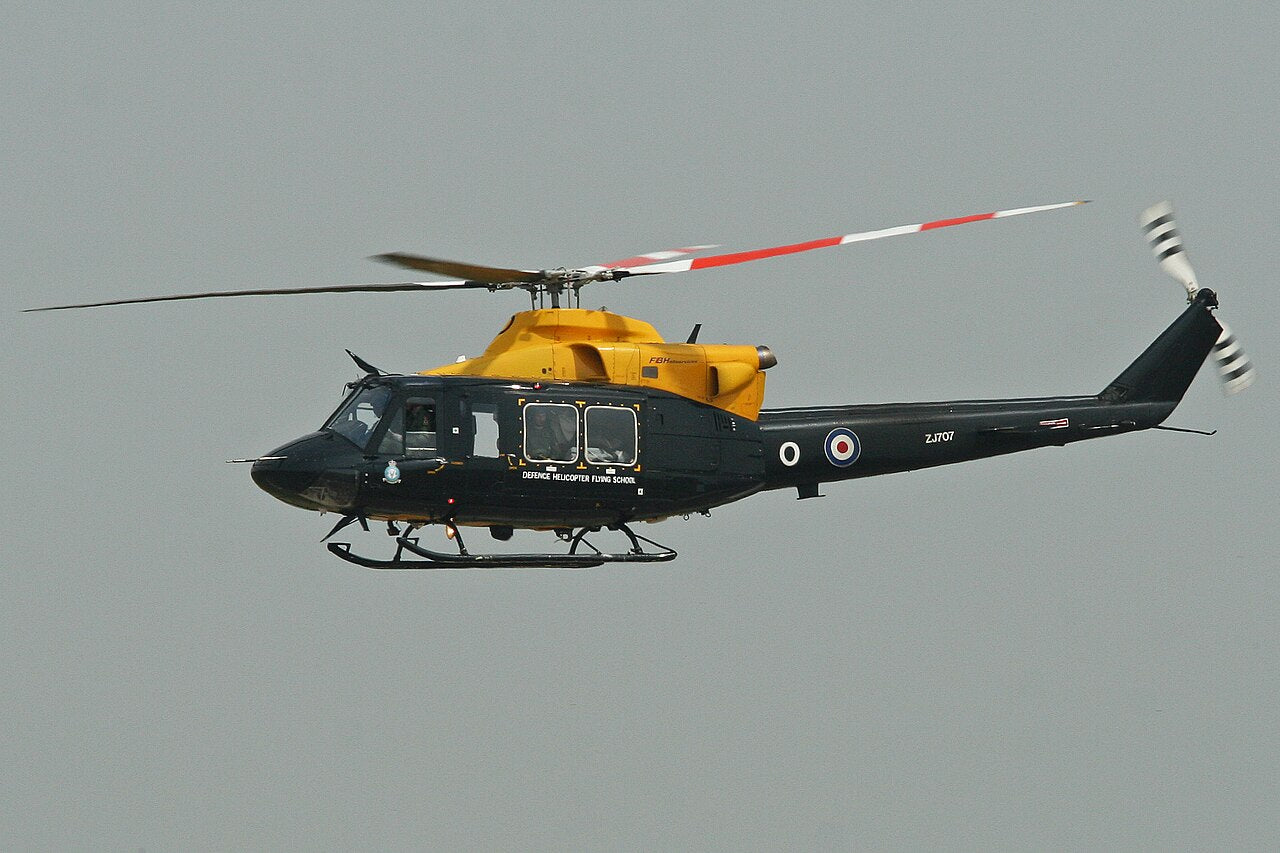 Black and yellow Griffin helicopter in flight, seen from the side with its complete visible main rotor, long tail, tail rotor and skids.