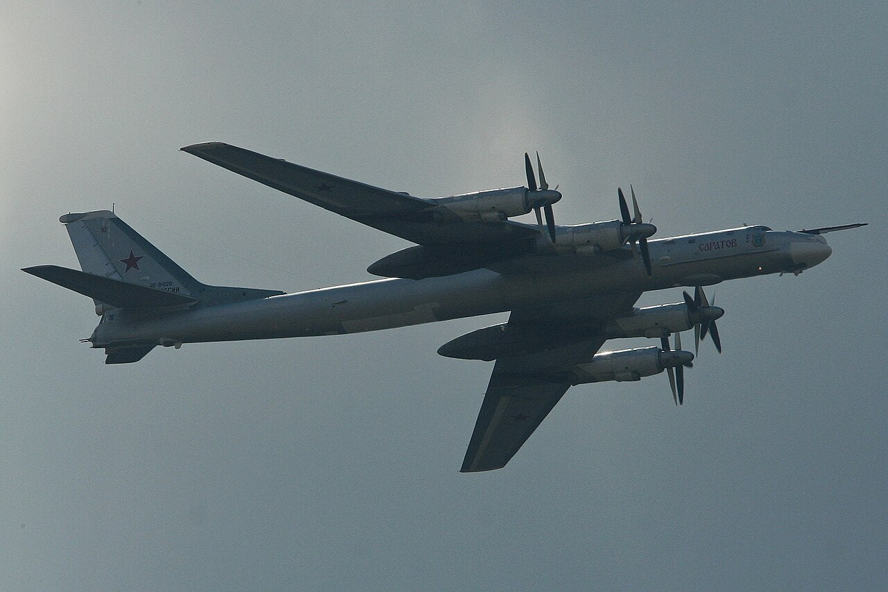 Tu-95MS seen from below in flight, showing four turboprop engines, swept wings, long fuselage and single fin.