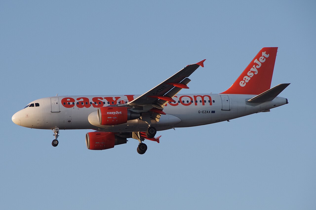 Orange-and-white Airbus A319-111 G-EZAX approaching to land, with two underwing engines and landing gear extended.