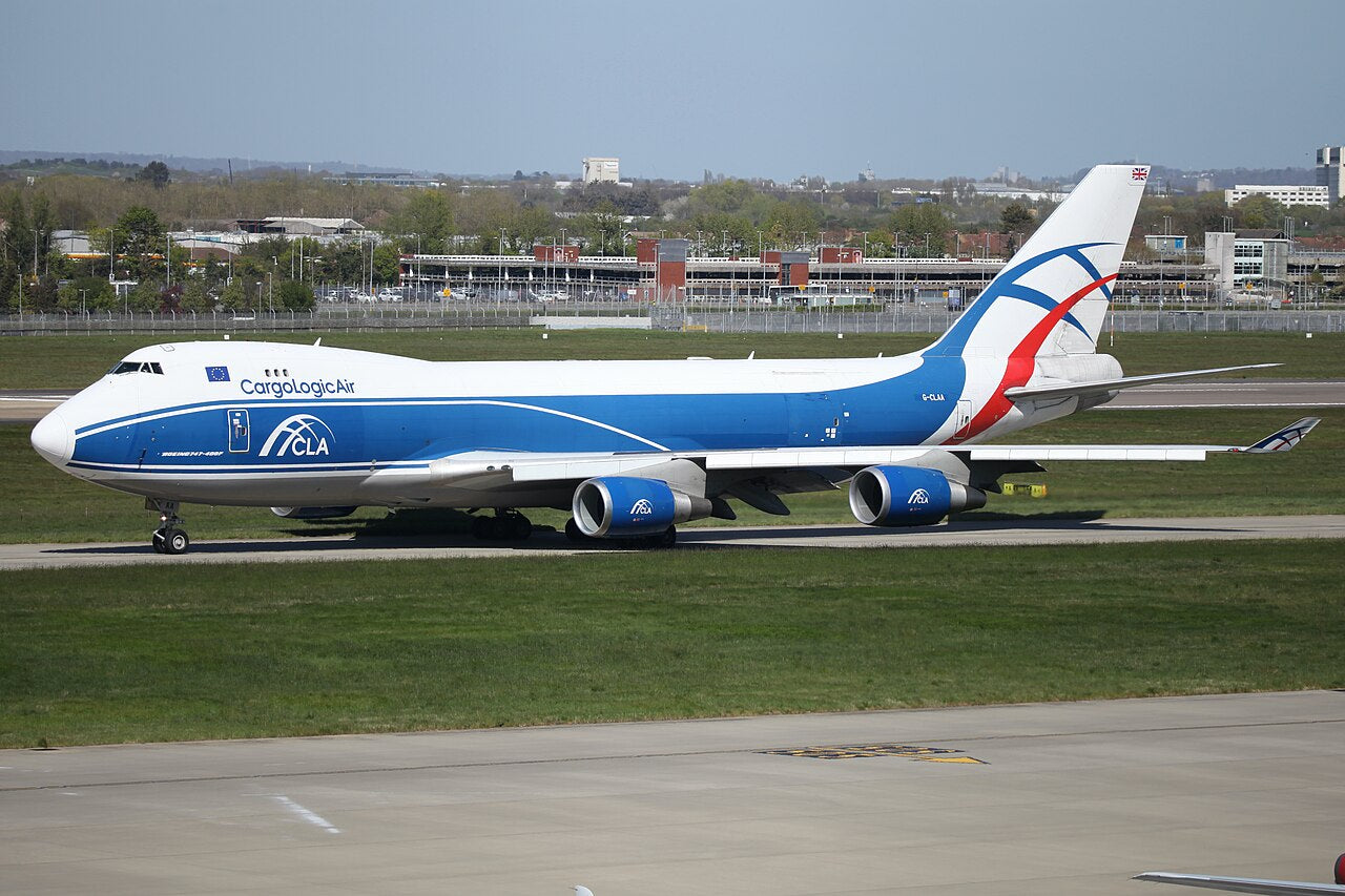 Blue-and-white CargoLogicAir Boeing 747-446F G-CLAA seen from the side at Heathrow, with its short upper deck, wings and landing gear visible.
