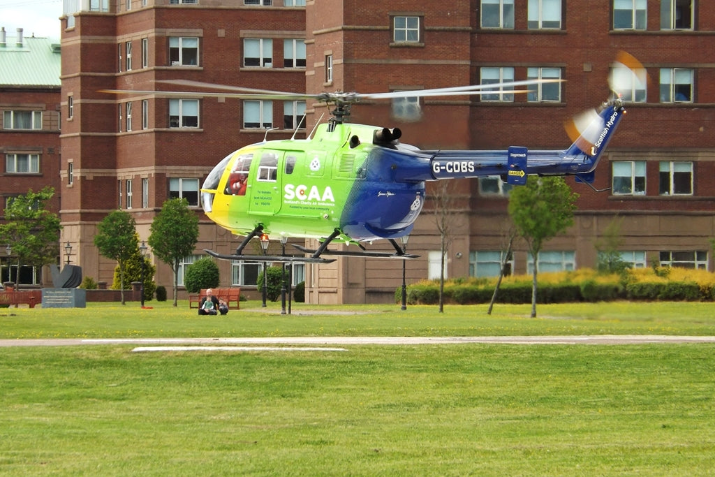 Green and blue MBB Bo 105 DBS-4 G-CDBS hovering, with the fuselage, tail, rotor span and skids in view.